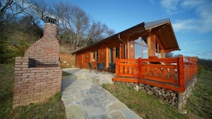 A wooden cabin with a stone chimney, a porch with a wooden railing, and a stone pathway leading to the entrance.