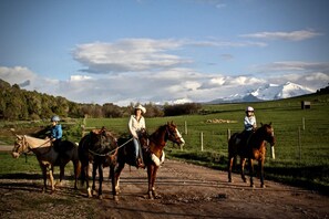 Four people riding horses on a dirt path with a green field and a mountain in the background. - Pet-Friendly and Gorgeous Safari Tent for a Glamping Getaway near White River National Forest, Colorado (Carbondale)
