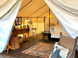 A tented accommodation with a bed, a small table, a chair, and a rug.