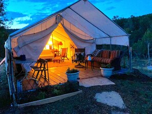 A tent with a warm interior light, a wooden deck, and a sofa outside.