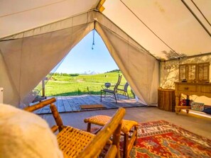 A tent with a view of a grassy field, wooden chairs, a rug, and a wooden cabinet.
