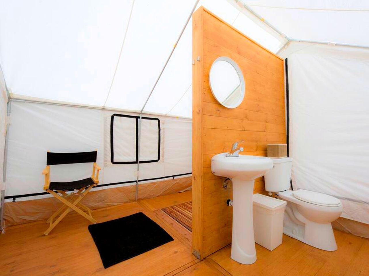 A tent with a wooden interior, a foldable chair, a sink, and a toilet.