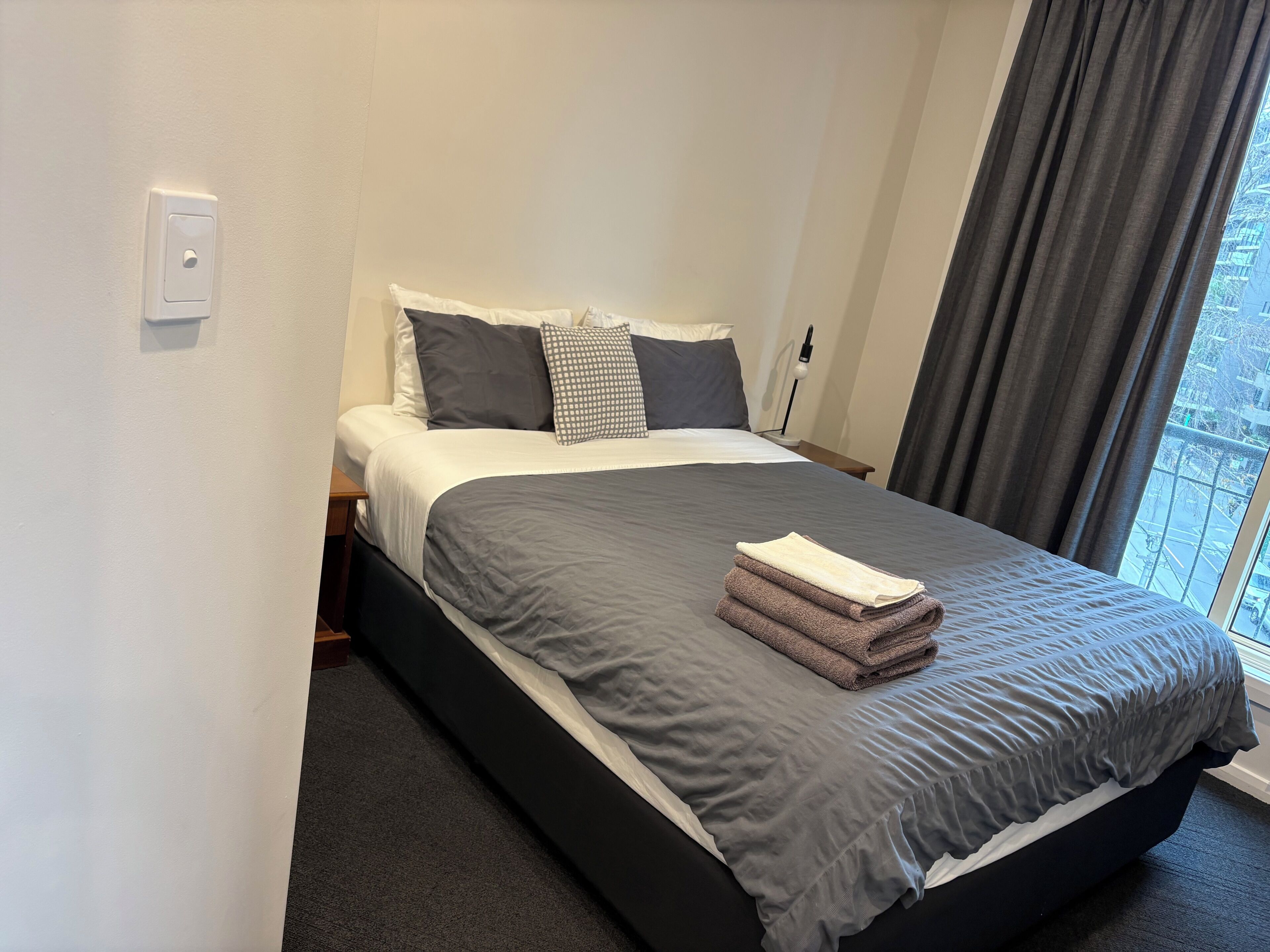 A hotel room with a bed, a nightstand, a lamp, and a window with curtains.