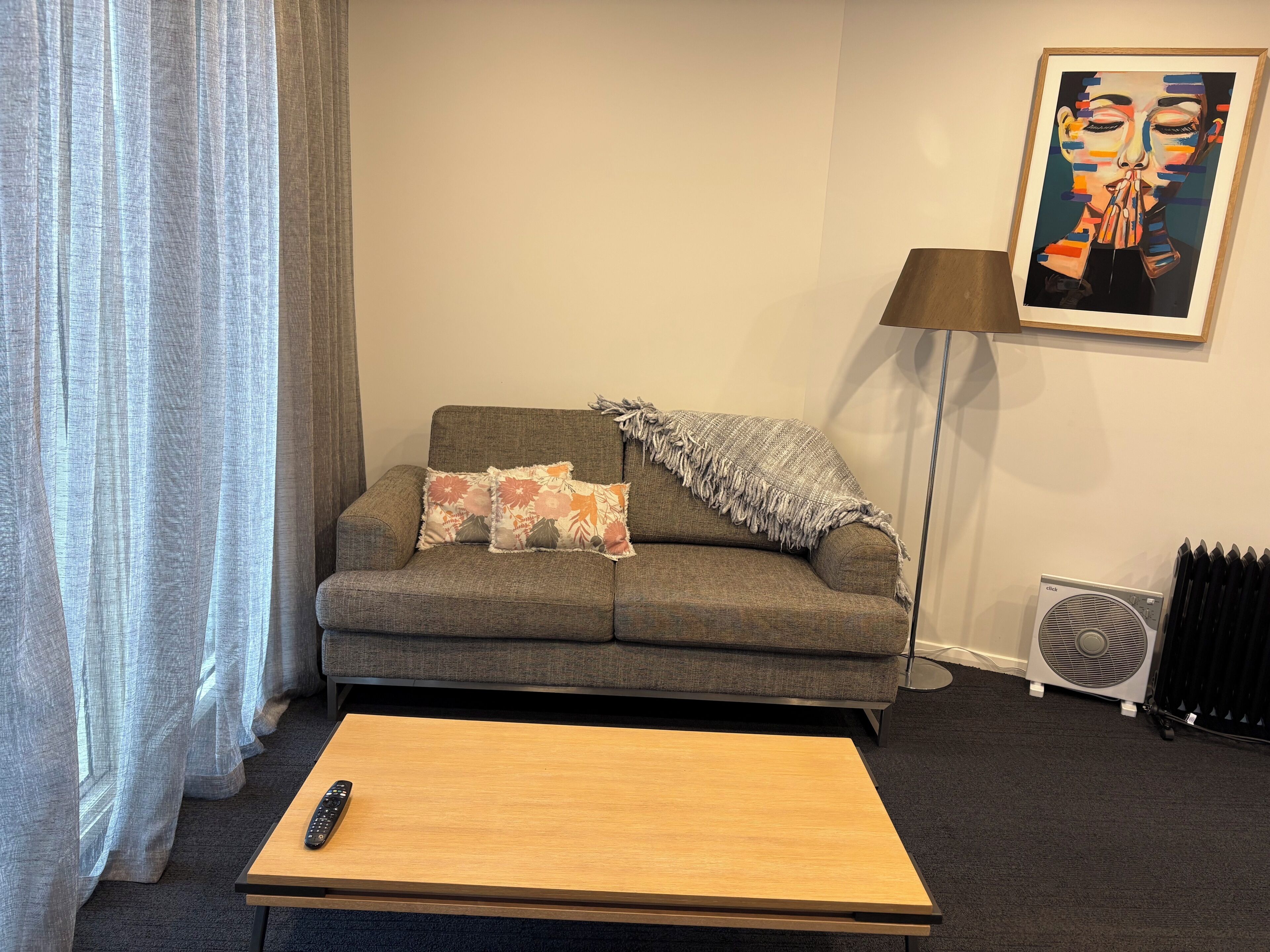 Ein Wohnzimmer mit einer Couch, einem Couchtisch, einer Fernbedienung, einer Heizung und einem Bild an der Wand.