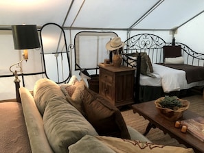 A tented accommodation with a bed, a sofa, a table with candles, and a lamp.