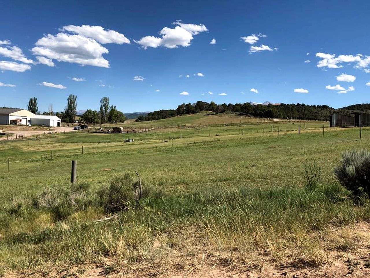 Ländliche Landschaft mit einem eingezäunten Feld, einem Gebäude und blauem Himmel.