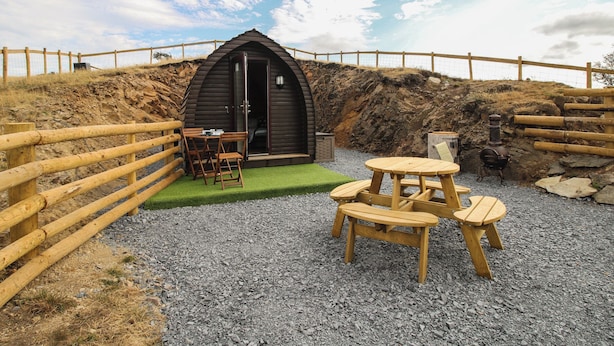 Uma cabana rústica de madeira com entrada circular, uma mesa de jantar com cadeiras e um fundo de parede de pedra.