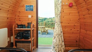 Interior acolhedor de uma cabana, com decoração em madeira, um aviso de segurança, uma janela com vista para o exterior e uma mesa com cadeiras do lado de fora.
