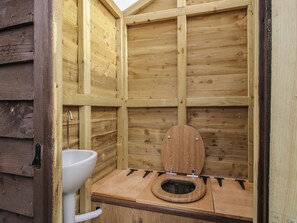 Eine hölzerne Gartenlaube mit einem weißen Waschbecken und einer Holzwc.