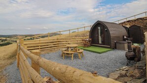 A rustic outdoor seating area with a wooden table and chairs, a small wooden structure, and a gravel ground.