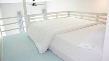 A single-bed room with a white ceiling fan, white walls, and a light blue floor.