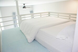 Habitación con cama individual, ventilador de techo blanco, paredes blancas y piso azul claro.