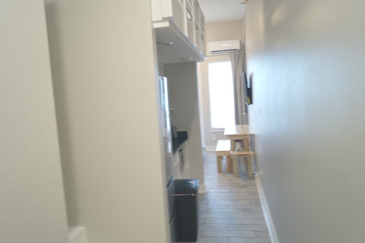 Un pasillo estrecho con suelo de madera, un banco y una puerta que da a otra habitación.