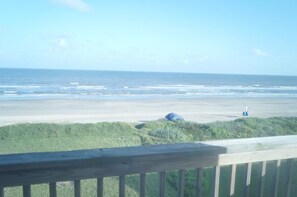 A beach view from a wooden deck with a railing, ocean waves, and a distant figure.