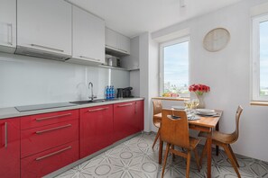 Una cocina moderna con armarios rojos, una encimera de acero inoxidable y un comedor con mesa lista para dos.