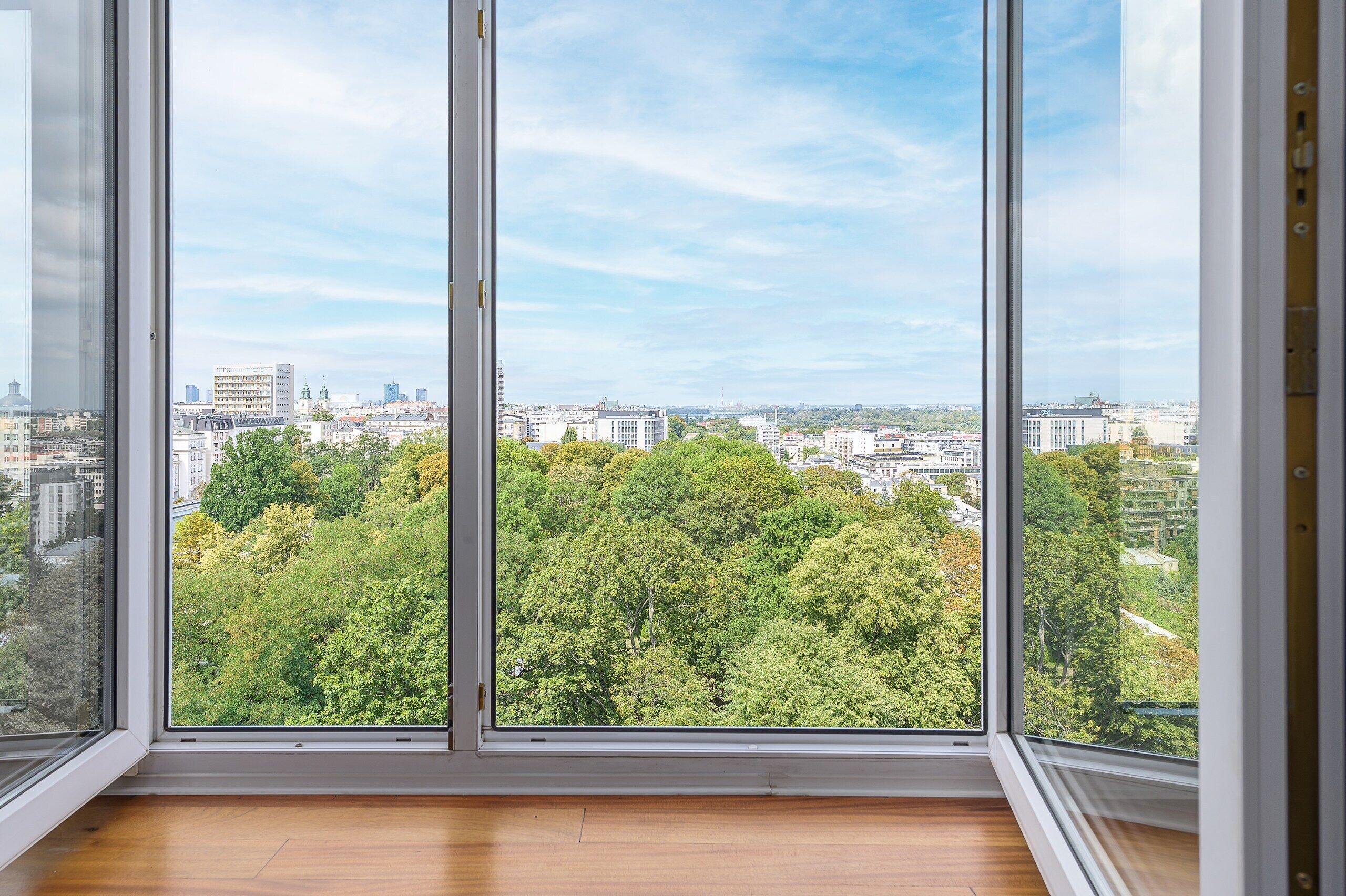 A room with large windows offering a view of a cityscape and dense greenery.