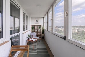 Ein schmaler Balkon mit Blick auf eine Stadtansicht, eine kleine Sitzecke mit Tisch und ein Bücherregal mit Pflanzen.