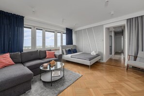 Uma sala de estar moderna com um sofá, uma cama, uma mesa de centro de vidro e vista através de janelas amplas.