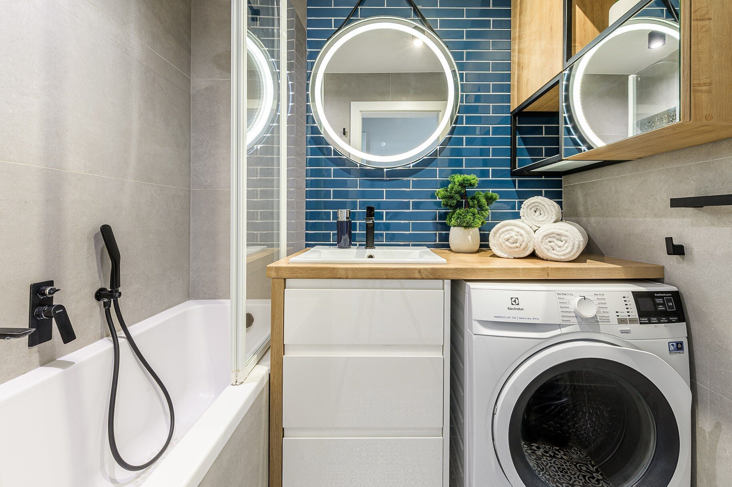 A modern bathroom with a bathtub, a washing machine, a sink with a mirror, and a small potted plant.