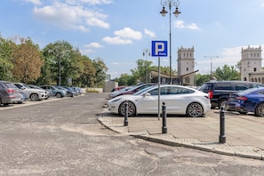 A parking area with a white car parked in front of a blue parking sign. - Lumina 3room Apart with Balkony & Center (Warszawa)