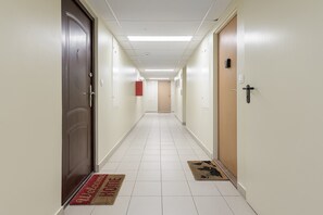 Um corredor de hotel com portas em ambos os lados, um tapete de entrada vermelho e bege e um chão de azulejos claros.