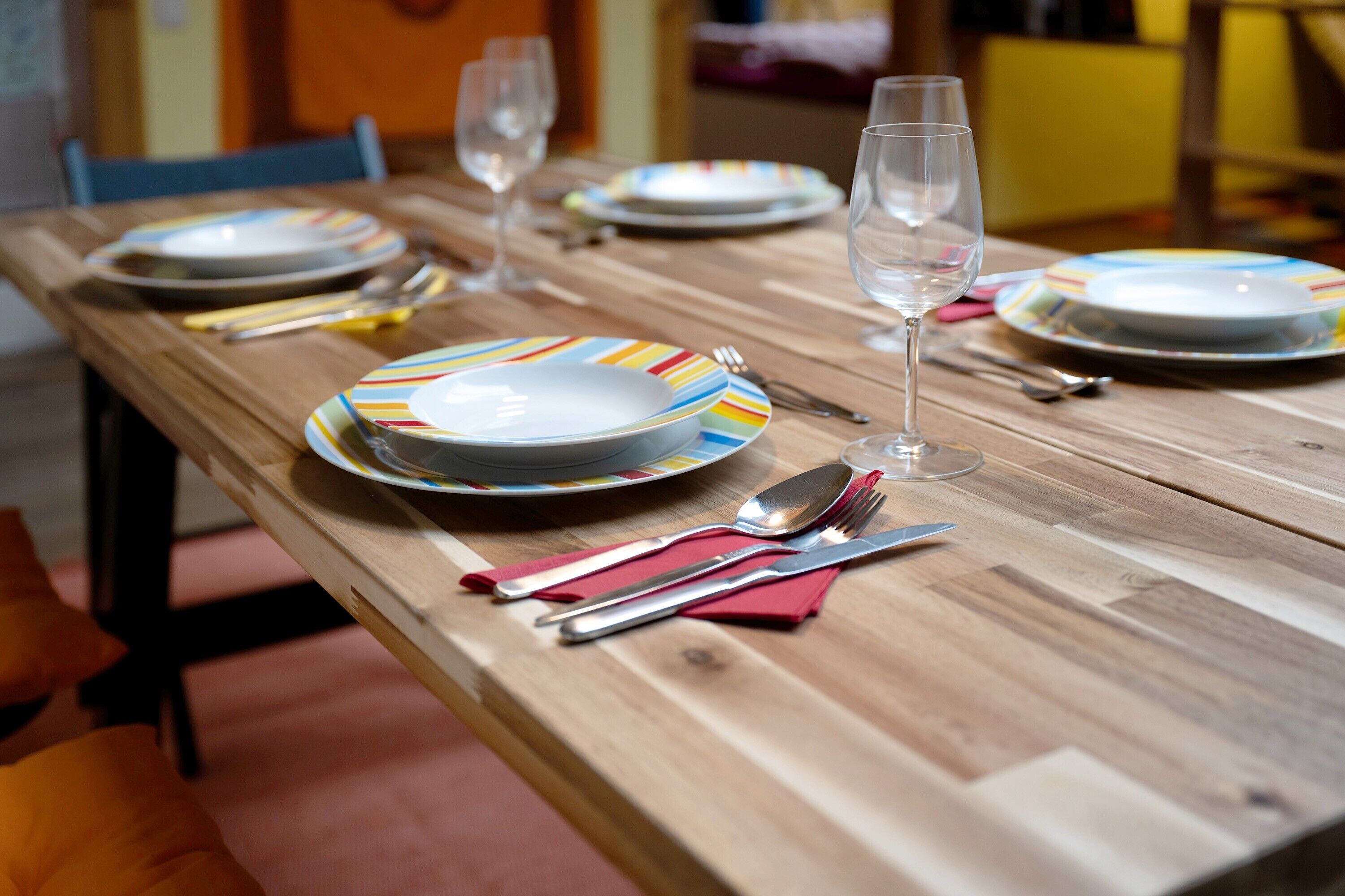 Une table de salle à manger en bois, mise avec des assiettes, des couverts et un verre.