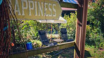 Une terrasse en bois avec une pancarte sur laquelle on peut lire « BONHEUR », une table, deux chaises et un parasol suspendu.