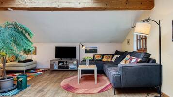 Ein gemütliches Wohnzimmer mit einer Couch, einem Fernseher und einer großen Pflanze.
