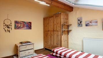 Ein Schlafzimmer mit Holzschrank, einem Bett mit gestreifter Bettwäsche, einem Traumfänger und zwei Wandbildern.