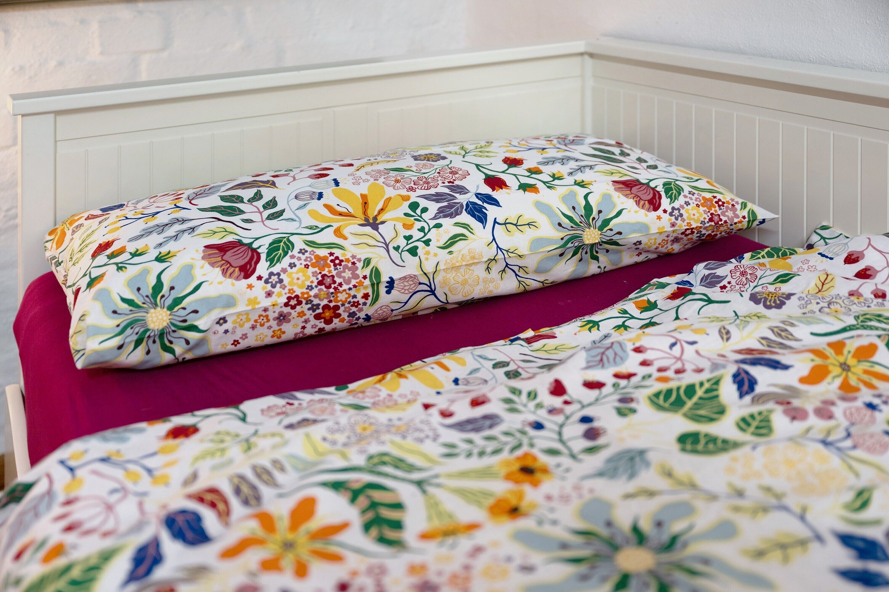 A bed with a floral-patterned duvet and pillows, a white headboard, and a purple bedspread.