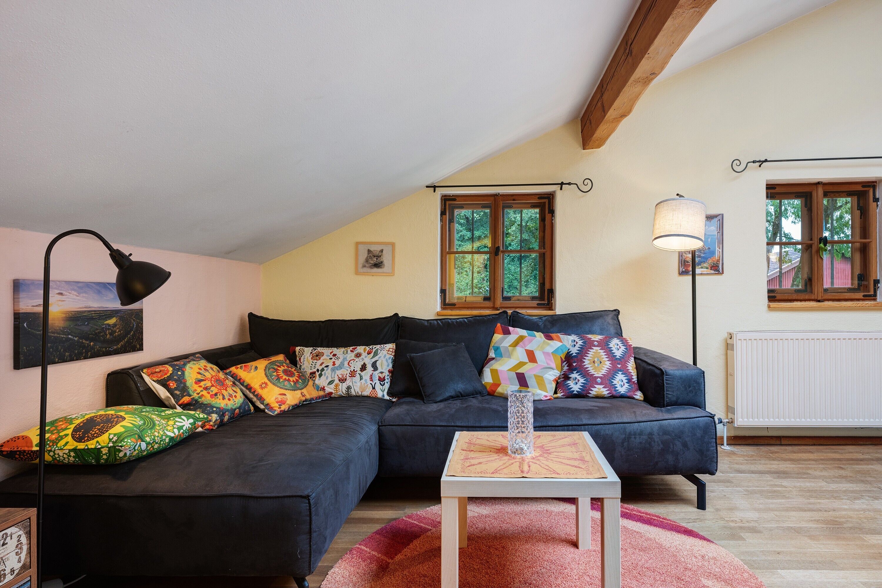 A cozy living room with a dark sofa, colorful cushions, a small table, and a painting.