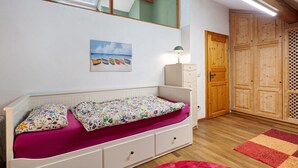 Un dormitorio con cama blanca, colcha estampada con flores, un cuadro de barcos en la pared, un armario de madera y una alfombra roja.