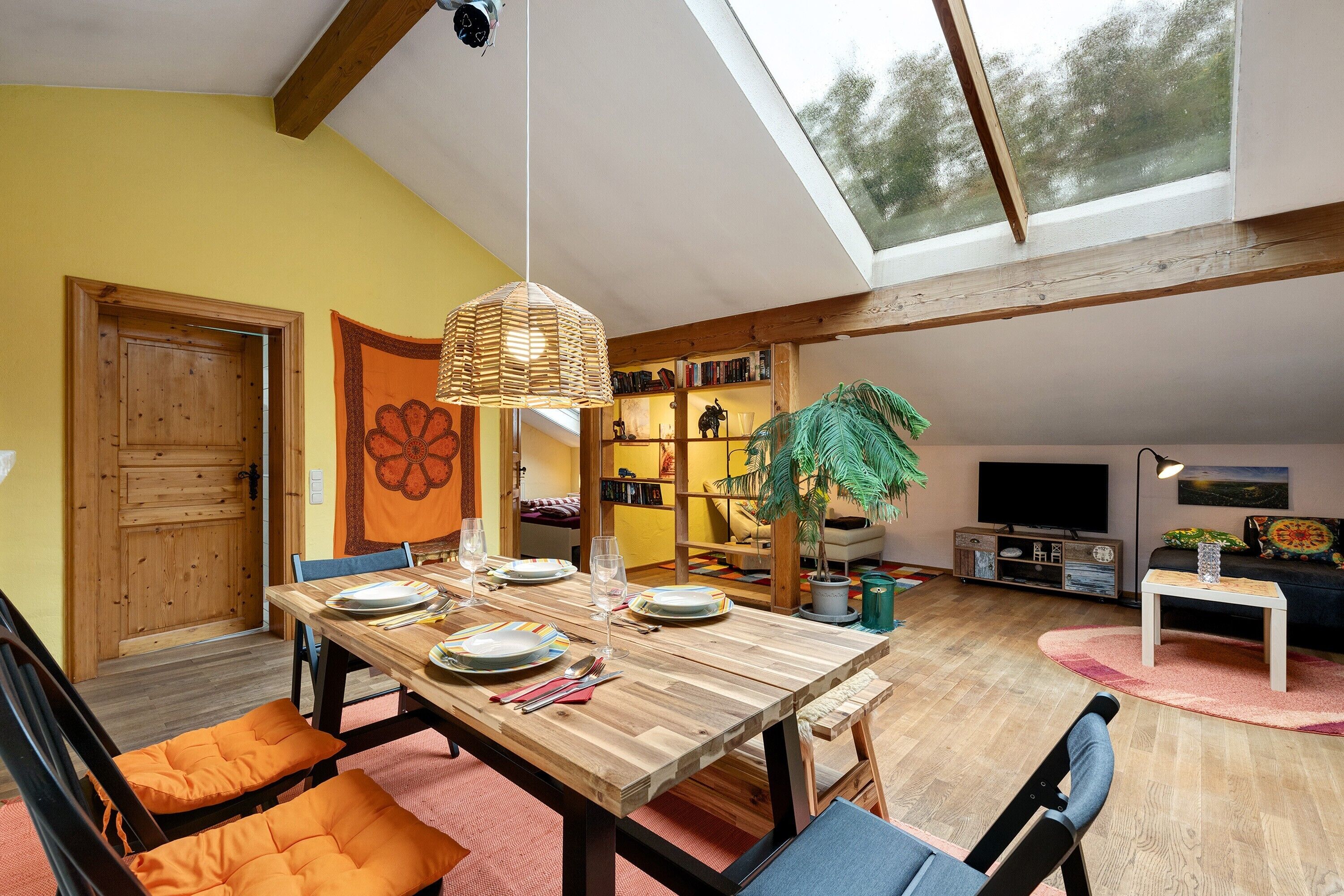 A dining area with a wooden table, orange cushions, and a hanging light fixture.