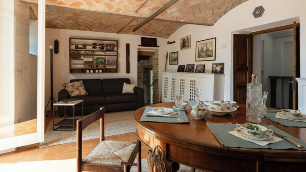 A cozy living room with a fireplace, a dining table set with plates and glasses, and a bookshelf with various items.