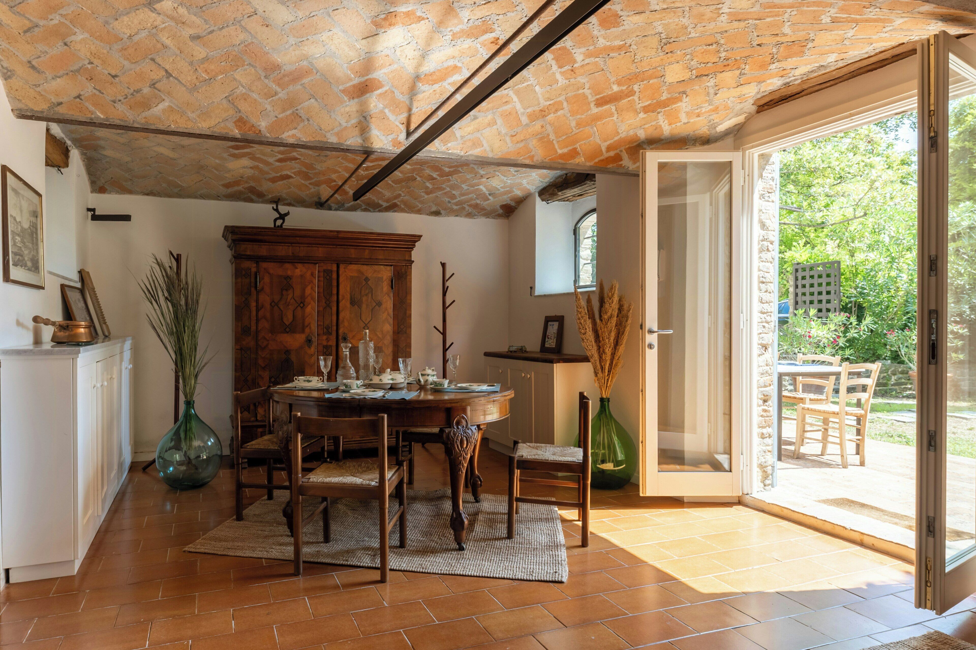 A dining area with a brick ceiling, a wooden table set for four, and a view through a glass door to an outdoor garden.