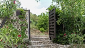 A stone staircase leading to a gated entrance with a lattice door, surrounded by lush greenery and potted plants.