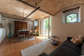 A spacious living area with a brick ceiling, a dining table set, a sofa, and a view through a glass door to an outdoor patio.
