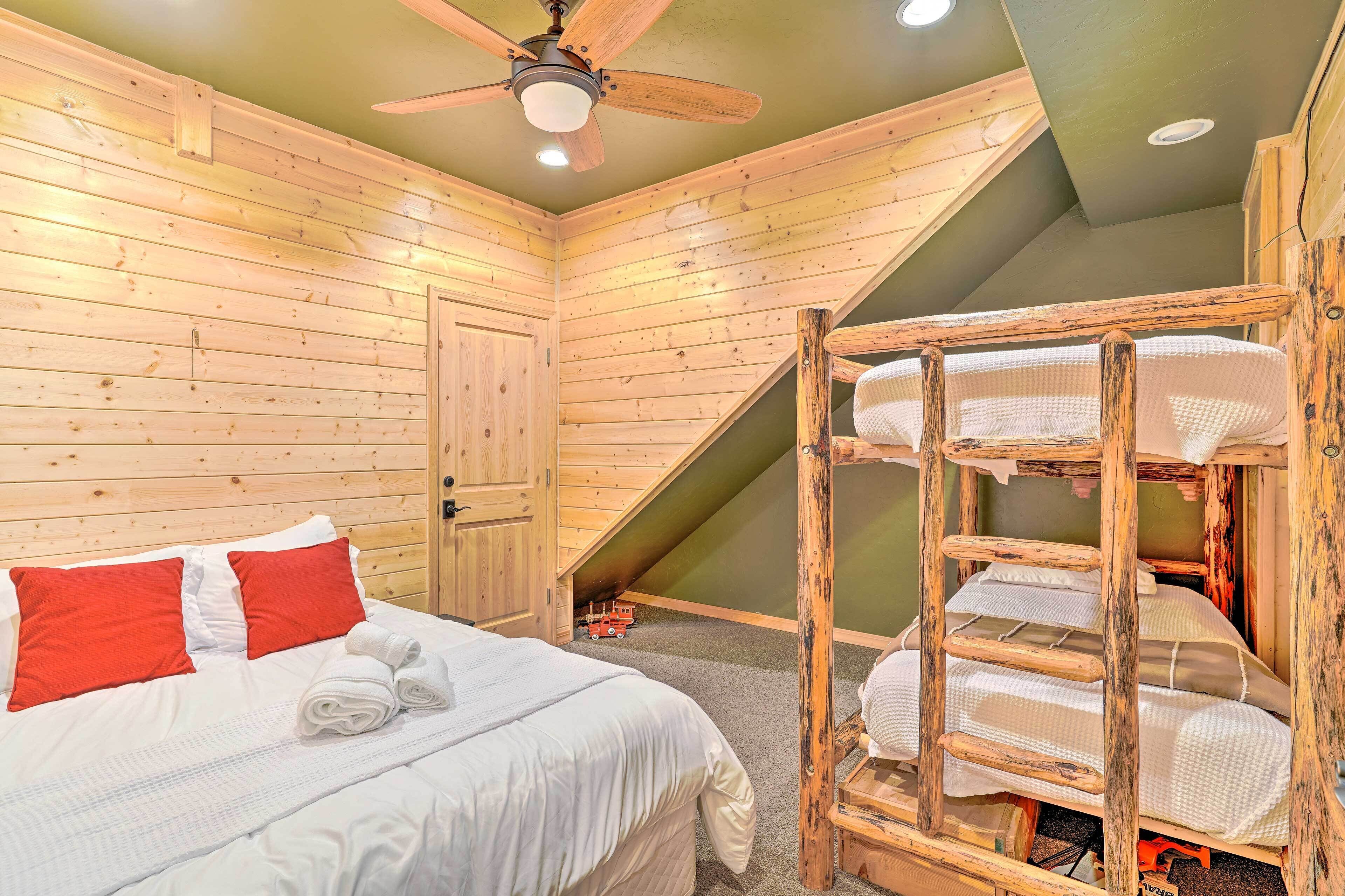 A wooden room with a bed, a bunk bed, a ceiling fan, and a door.
