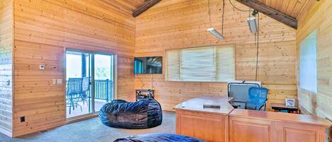A log cabin interior with a ceiling fan, a large window with blinds, a television, and a desk with a chair.