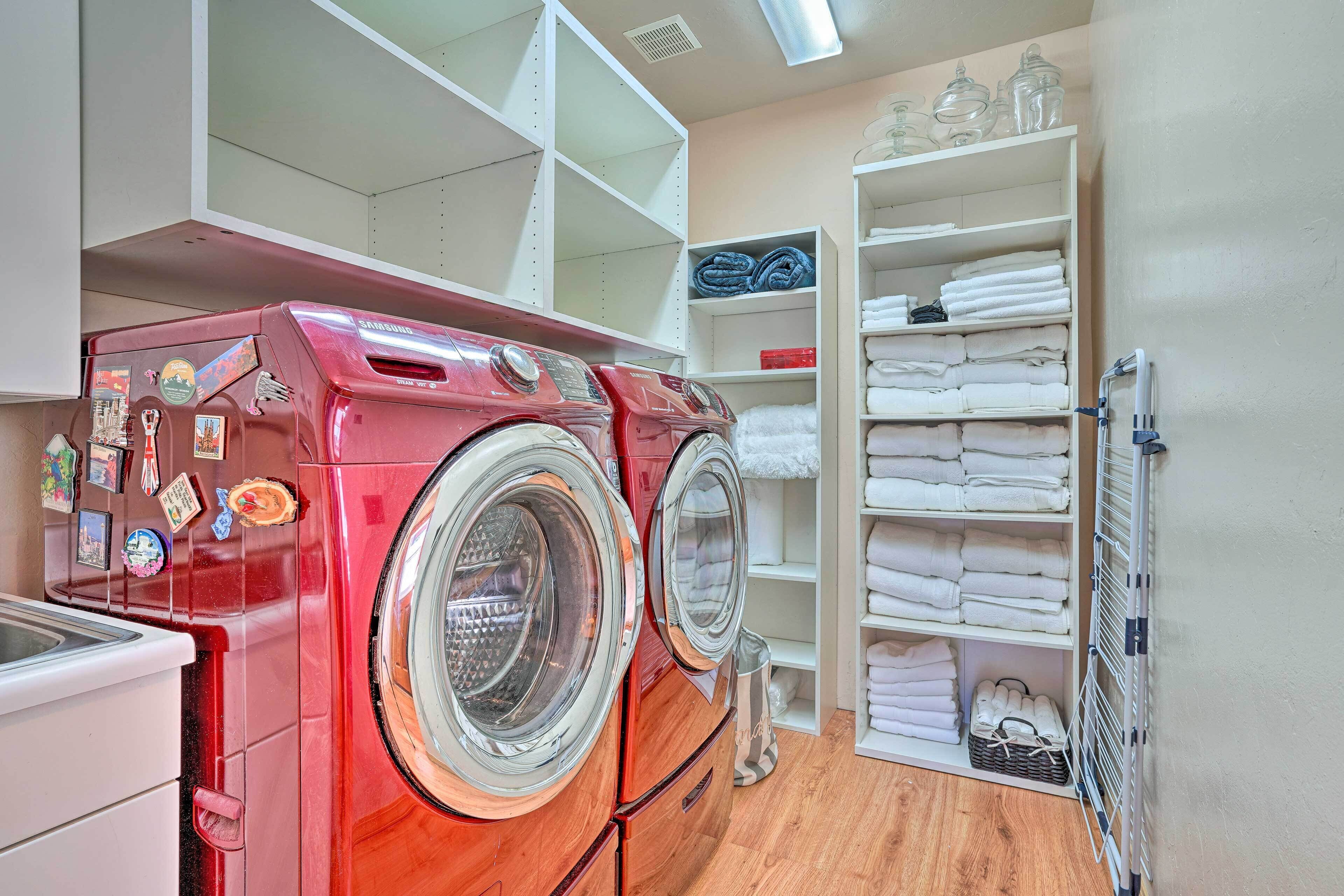 A laundry room with two red front-loading washing machines, a white drying rack, and shelves with neatly folded towels.