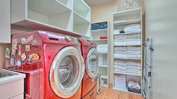 A laundry room with two red front-loading washing machines, a white drying rack, and shelves with neatly folded towels.