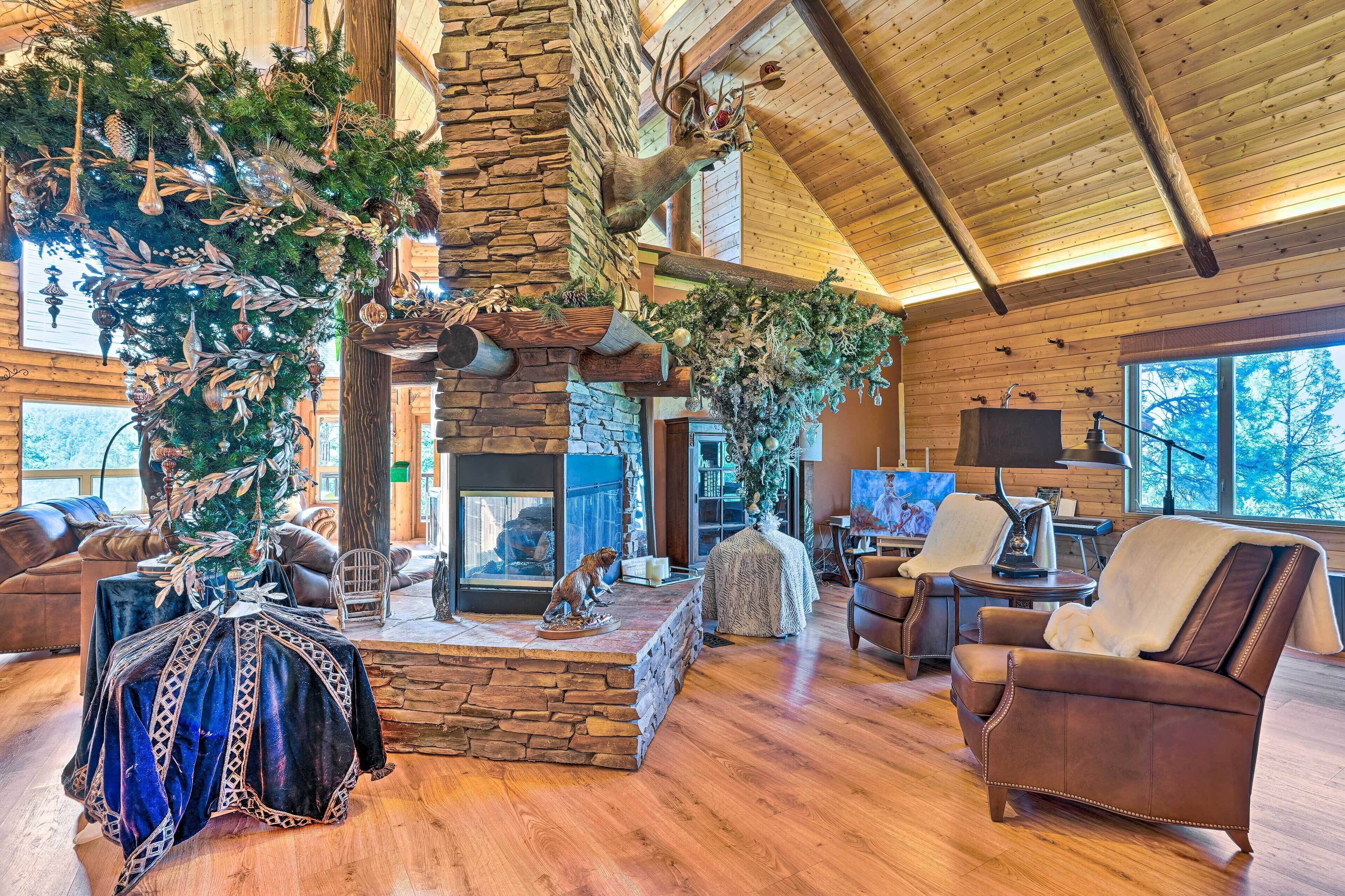 L’intérieur d’une cabane en rondins, avec une cheminée en pierre, des meubles en cuir et un grand arbre décoré d’ornements.