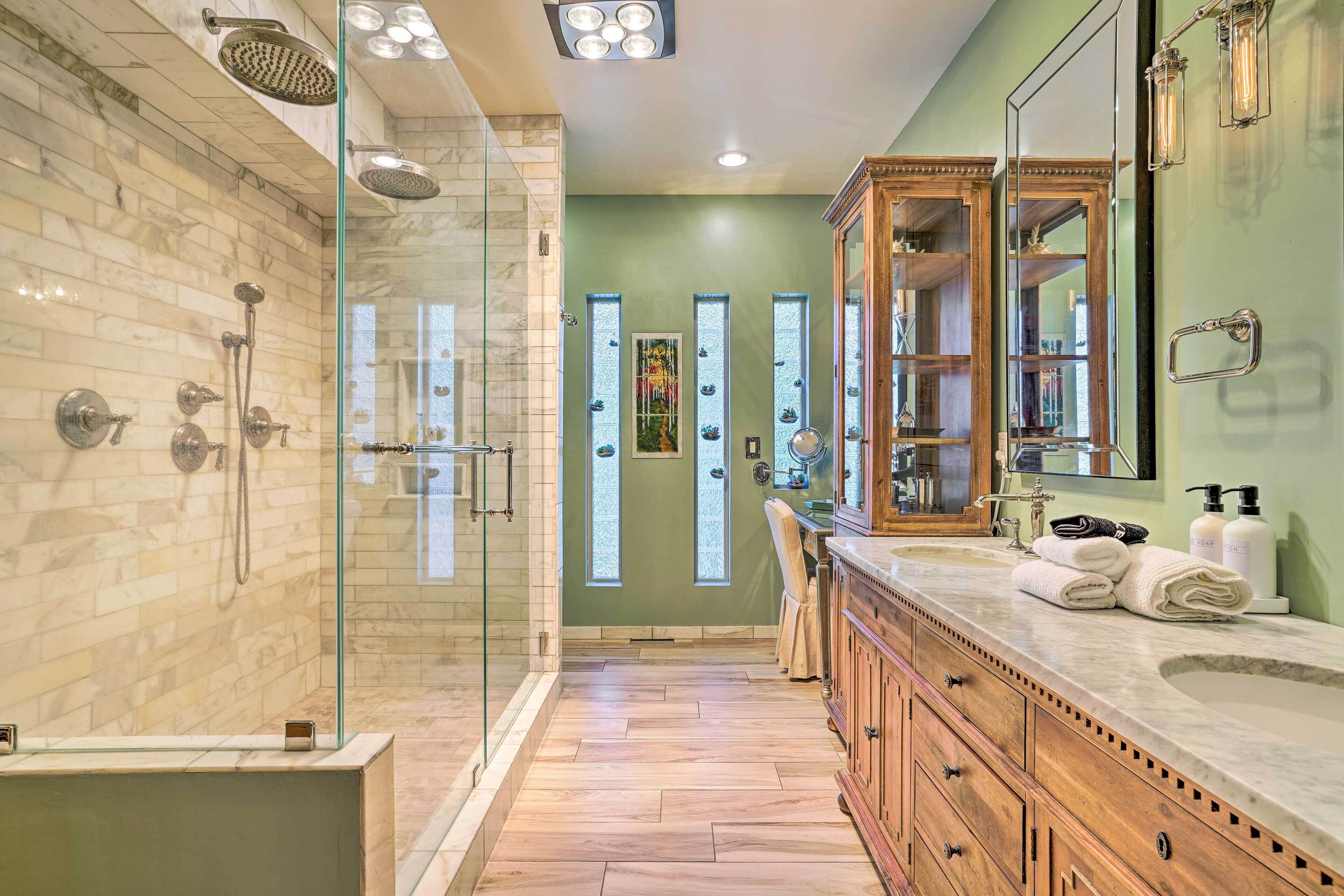 Un baño moderno con ducha envuelta en vidrio, tocador con espejo grande y mueble de madera.