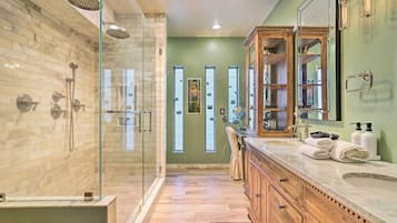 Un baño moderno con ducha envuelta en vidrio, tocador con espejo grande y mueble de madera.