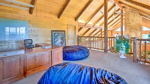 Une pièce spacieuse avec un plafond en bois, un bureau, une chaise, un grand fauteuil en forme de poire et une vue sur l’extérieur.