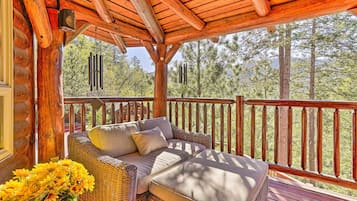 Una terraza de madera con un sofá de mimbre y cojines, con vistas a un área boscosa.
