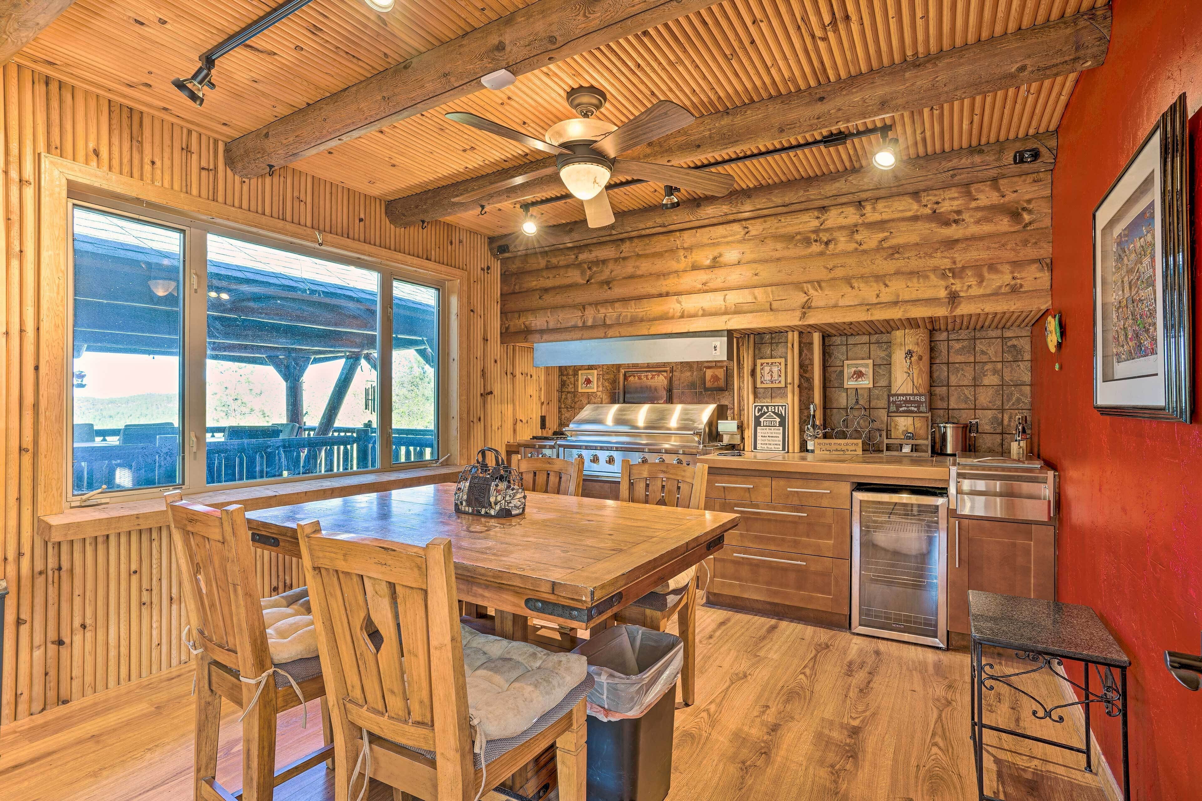 Un interior de madera con una mesa de comedor, sillas, una zona de cocina y un ventanal con vistas a una terraza exterior.