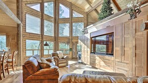 A spacious living area with a large window, leather sofas, and a flat-screen TV. - Luxe Prescott Natl Forest Home w/ Huge Deck (Prescott)