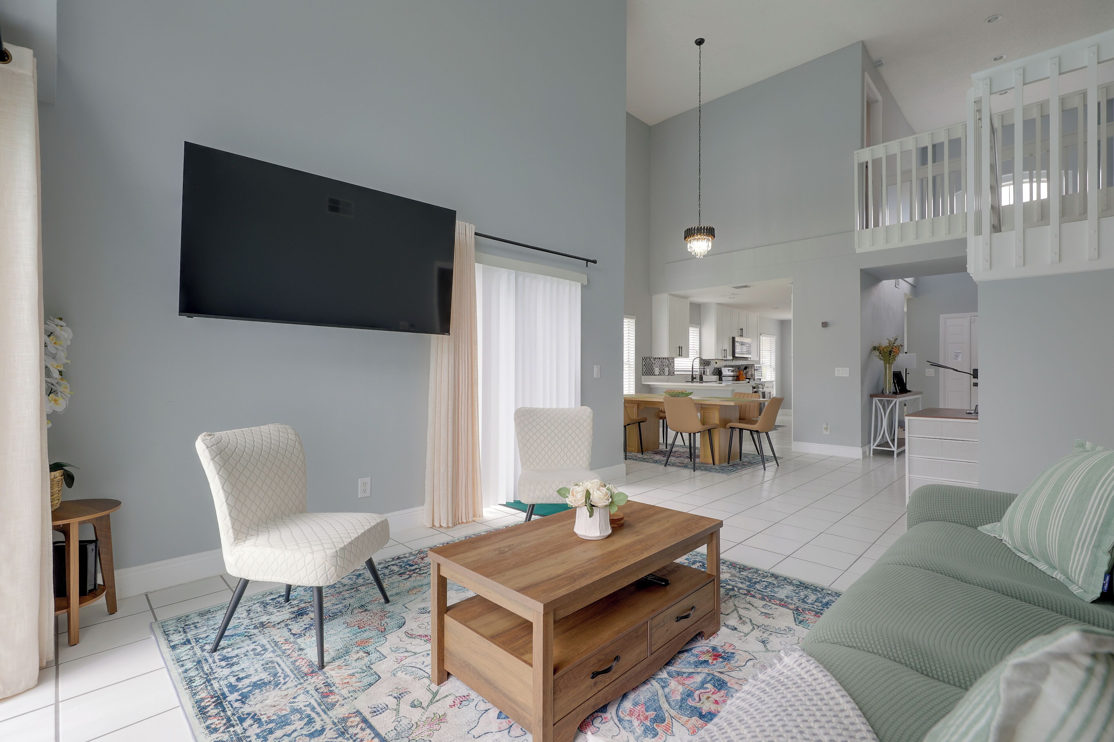 A spacious living room with a flat-screen TV, a wooden coffee table, and a green sofa.