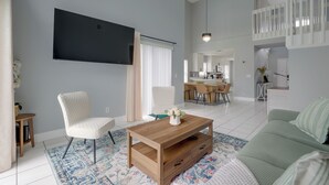 Ein geräumiges Wohnzimmer mit einem Flachbildfernseher, einem Holztisch und einem grünen Sofa.